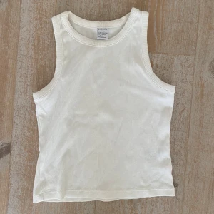 Vit ribbad linnetopp från Lindex - Säljer en enkel och stilren vit ribbad linnetopp från Lindex Kids. Toppen är ärmlös och har rund halsringning, perfekt för varma dagar eller som lager under andra plagg.