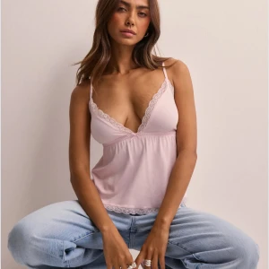 Ljusrosa linnetopp med spets från Nelly - Söt ljusrosa linnetopp från Nelly med tunna axelband och v-ringning. Toppen har fina spetsdetaljer längs urringningen och nederkanten. Perfekt för sommardagar eller som ett lager under en kofta. Slutsåld på nätet 