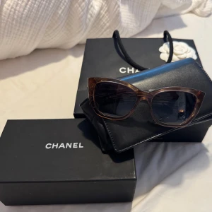 Bruna solglasögon från Chanel - Snygga bruna/rosa solglasögon från Chanel med en elegant design. De har en klassisk form och mörka linser som ger ett stilrent intryck. Perfekta för att lyfta din look med en touch av lyx. Kvitto och alla möjliga tillbehör finns. 