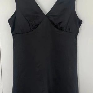 Svart klänning - Elegant svart klänning i satintyg. Helt oanvänd med lappen kvar! Perfekt till mösspåtagning eller till festlighet! 