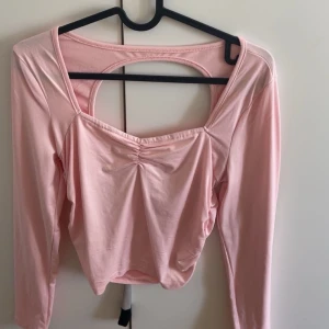 Rosa långärmad topp med öppen rygg - Säljer en söt rosa långärmad topp med en stilren öppen rygg. Toppen har en rynkad detalj framtill som ger en fin passform. Perfekt för en trendig look!