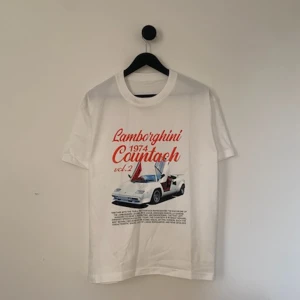 Laidback T-shirt  - Snygg vit t-shirt med stort tryck av en Lamborghini Countach från 1974 på framsidan. Texten är i rött och motivet visar bilen med öppna dörrar. Perfekt för bilentusiaster som vill sticka ut med en cool och retroinspirerad look. 