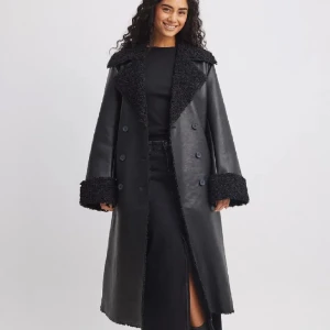 Svart kappa med pälsdetaljer - Helt ny PU kappa med teddy detaljer från NAKD, pris lapp är kvar. Den är jätte varm. anledningen till varför jag säljer den är för att den är för stor för mig och mitt öppet köp har gått ut, köpte den för 3 veckor sen. Pris kan diskuteras.