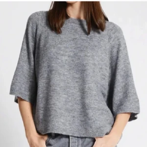 Grå stickad tröja - Säljer en mysig grå stickad tröja med trekvartsärm. Perfekt för kyligare dagar och enkel att matcha med olika outfits. Tröjan har en avslappnad passform och rund halsringning.