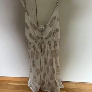 Vit kortklänning med beige mönster - Söt vit kortklänning med beige mönster och smala axelband.🩷