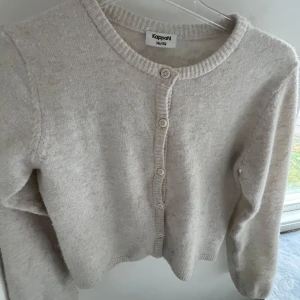 Beige stickad kofta från Kappahl - Mysig beige stickad kofta från Kappahl med rund halsringning och knappar framtill. 