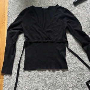 Svart omlottopp från Saint Tropez - Snygg svart omlottopp från Saint Tropez, man kan knyta jättefint där bak med hjälp av knappar, eller så kan man bara knyta en vanlig rosett👌säljer för att den är för stor