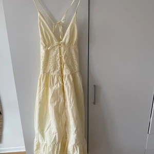 Ljusgul långklänning med broderade detaljer - Söt ljusgul långklänning från mango med smala axelband och v-ringning. Klänningen har broderade blommönster på överdelen, knytning fram och knappdetaljer. Jättefin knytning även i ryggen.Perfekt för varma dagar och somriga tillfällen.
