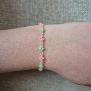 Sött armband med små blommor i rosa och grönt - Handgjort Armband med små blommor i pärlliknande material i rosa och grönt på en tunn silverfärgad kedja. Perfekt för att addera en färgglad och lekfull touch till din stil.