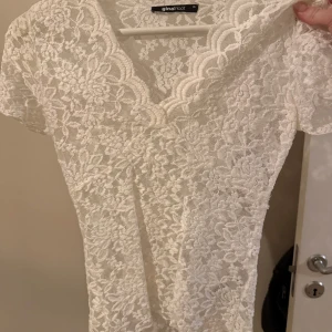 Vit spetsblus från Gina Tricot - Säljer en superfin vit spetsblus från Gina Tricot i storlek XS. Blusen har korta ärmar, v-ringning och är helt täckt av blommig spets. Perfekt att styla med jeans eller kjol för en fräsch look!