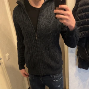 Mörkblå Cardigan - Säljer en tjockare mörkblå cardiganmed dragkedja framtill. Tröjan har ett snyggt mönster och långa ärmar med ribbade muddar. Perfekt för kyligare dagar.