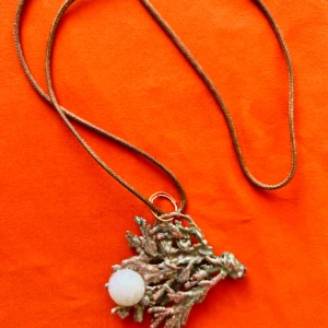 Halsband med korallinspirerad hänge och pärldetalj - Unikt halsband med ett korallinspirerat hänge i metall och en rund vit pärldetalj. Hängs på en tunn brun läderrem. Perfekt för dig som gillar naturinspirerade smycken och vill sticka ut.