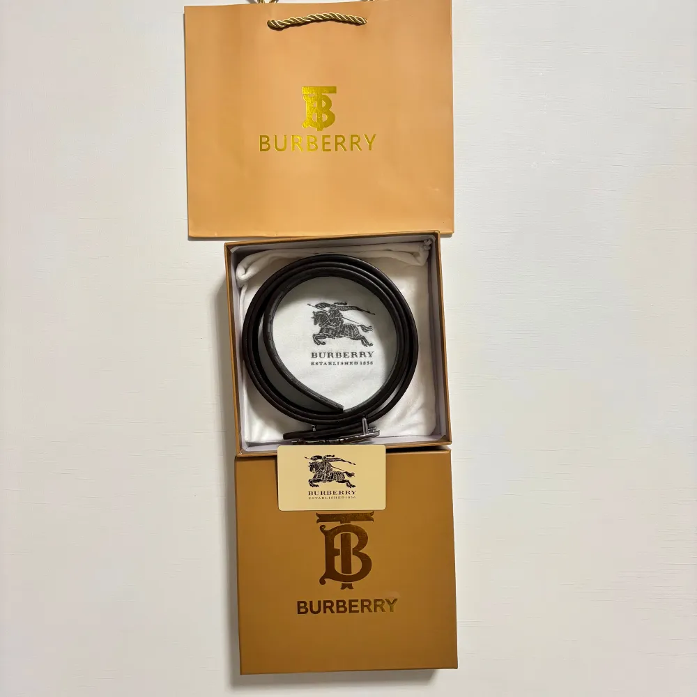 Snyggt bälte från Burberry med klassiskt rutigt mönster i beige och bruna toner. Spännet är i silver och har en detaljrik design. Perfekt för att ge en stilren touch till din outfit.. Muu.