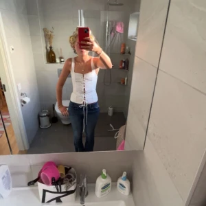 Vit korsett med snörning - Säljer en stilren vit korsett med smala axelband och snörning framtill. Perfekt för att skapa en elegant look. Passar bra till jeans eller kjol.