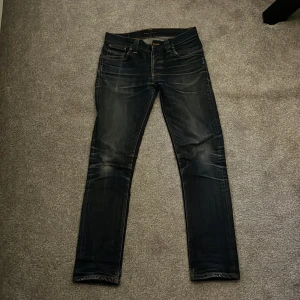 Nudie jeans grim Tim - Snygga mörkblå jeans från Nudie Jeans med en klassisk femficksdesign. De har en normal passform och är tillverkade i slitstarkt denim. Perfekta för en avslappnad stil.