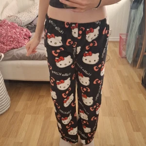 Svarta Hello Kitty byxor - Lågmidjade Mysiga svarta byxor med Hello Kitty-motiv i vitt och rött. Byxorna har en loose passform och är perfekta för en avslappnad dag hemma. De är dekorerade med söta Hello Kitty-ansikten och röda rosetter. Skulle även tro att de passar någon med S 