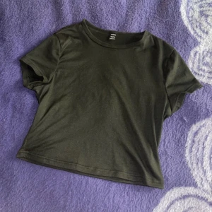 Svart croppad t-shirt från SHEIN - En enkel svart croppad t-shirt från SHEIN. T-shirten har rund halsringning och korta ärmar, perfekt för en avslappnad stil. Passar bra till jeans eller kjol för en clean look.