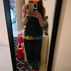 Färgglad långbyxor o Line med regnbågsmönster - Säljer en långbyxor o line med svart överdel och färgglad nederdel i regnbågens färger. Klänningen har smala axelband och ett unikt mönster med små vita prickar. Perfekt för dig som vill sticka ut med en bohemisk och färgstark stil.