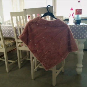 Rosa poncho med pärlor - Säljer en fluffig rosa poncho med små pärlor som detalj. Perfekt för att hålla sig varm och snygg under kyliga dagar. Mjuk och mysig känsla, passar till många outfits.