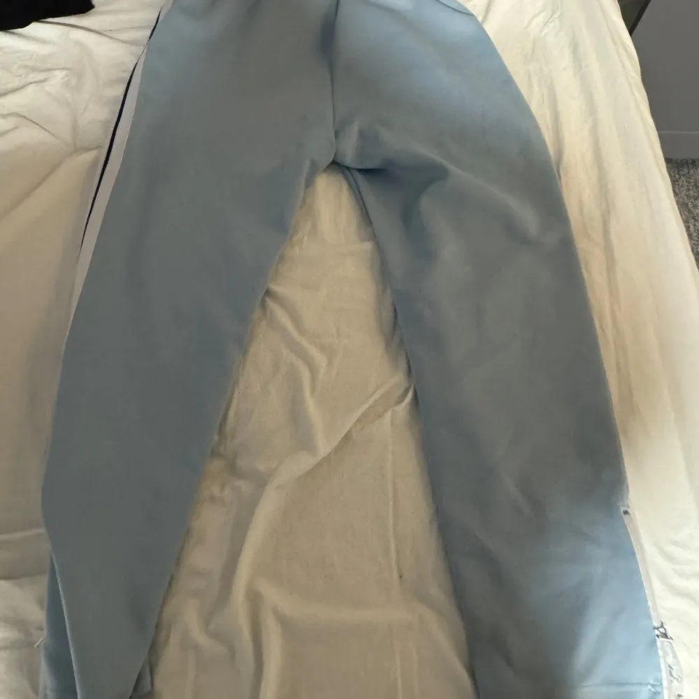 Snygga ljusblå byxor från Palm Angels med vita och svarta ränder längs sidorna. Byxorna har en avslappnad passform och är perfekta för en trendig look. Märkesloggan är tryckt på framsidan.. Farkut & Housut.