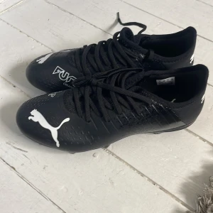 Svarta fotbollsskor från Puma - Säljer ett par svarta Puma Future Creator Zones fotbollsskor med vit logga. Skorna har snörning och är designade för optimal prestanda på planen. Perfekta för dig som vill ha stil och funktion i ett.. helt nya inte använt en gång storlek 40. Kan bli billigare pris vid en snabb affär