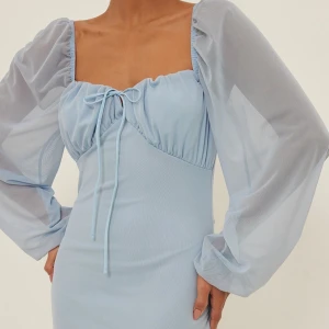 Slutsåld populär klänning från NA-KD - Supersöt ljusblå klänning från NA-KD med långa puffärmar i mesh och knyt framtill. Klänningen är från NA-KD och är helt slutsåld (går inte att få tag på längre). Inga defekter alls!:) bara använd på förra årets midsommar!