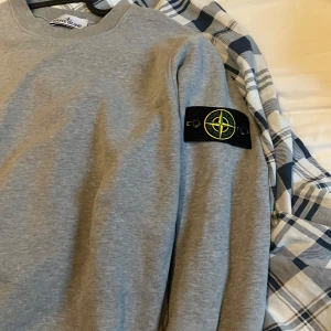Grå Stone Island sweatshirt M - Säljer en grå sweatshirt från Stone Island i storlek M. Tröjan har klassisk rund hals, lång ärm och den ikoniska Stone Island-loggan på vänster ärm. Tillverkad i mjuk bomull för skön komfort och stilren look.