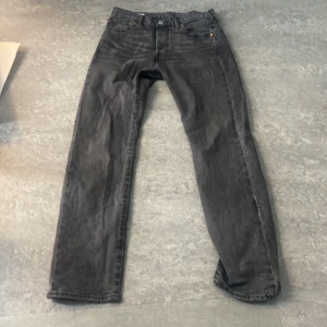 Levis 501 svarta jeans straight fit - Klassiska svarta Levis 501 jeans med rak passform och fem fickor. Jeansen har en mörk tvätt och är tillverkade i robust denim. Perfekta för dig som gillar en tidlös och avslappnad stil.