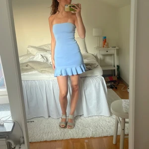 Ljusblå axelbandslös volangklänning - Superfin ljusblå kort klänning med axelbandslös design och volangkant nertill. Sitter tight och har en clean, enkel look som känns både söt och trendig. Gammal klänning från zara som inte säljs längre!