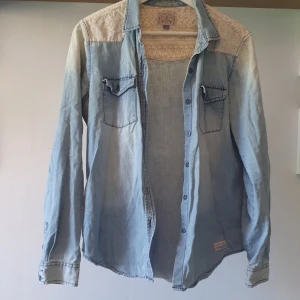 Ljus jeansskjorta Broken Arrow M - Snygg ljusblå jeansskjorta från Broken Arrow med mönstrade axelpartier i beige och vitt. Skjortan har två bröstfickor med lock och knappar framtill. Perfekt för dig som gillar en avslappnad och cool stil. 100% Bomull 