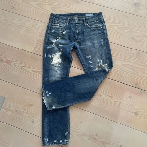 Vintage Jack&Jones jeans - Tjena, säljer detta par feta straight fit Jack and Jones jeans. Det står tyvärr inte storleken någon stans, men midjan är cirka 44cm, och längden (midja till slutet) cirka 108cm. Dom har en snygg design med slitningar vilket gör dom mer unika. Hör av er vid frågor eller funderingar!