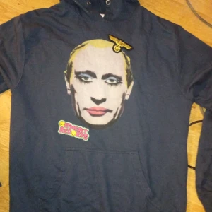 Prostitute Putin w custom patches - Mörkblå hoodie med stor, färgglad tryckt ansikte framtill och Offment Records-logga. Har huva och känguruficka. Unik detalj med broderad patch upptill. Perfekt för dig som vill sticka ut med din stil.