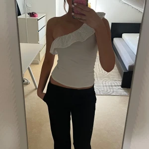 Vit oneshoulder topp med volang - Säljer vit topp med oneshoulder och volangkant i broderad spets. 