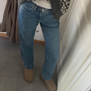Blå raka jeans i klassisk modell - Säljer ett par blå jeans med rak passform och låg midja. Jeansen har klassisk femficksdesign och är tillverkade i tåligt denimtyg. Perfekta för en avslappnad och tidlös look.
