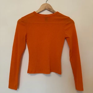 Orange långärmad topp  - Säljer orange långärmad topp från H&M. Perfekt för att liva upp garderoben med en färgklick. Är genomskinlig.