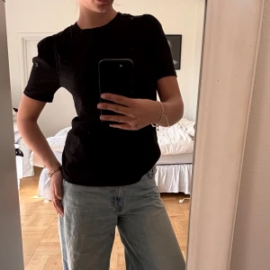 Svart ribbad topp med puffärm - En svart ribbad topp med korta puffärmar och rund halsringning. Snygg och enkel modell som är lätt att matcha till jeans eller kjol. Materialet är stretchigt och ger en bekväm passform. Perfekt för dig som gillar stilrena basplagg med en twist.