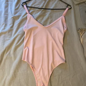 Ljusrosa body med v-ringning - Säljer en enkel och stilren ljusrosa body i onepiece-modell med smala axelband och v-ringad hals. ger en clean och fräsch look. Materialet känns mjukt och följsamt mot huden.