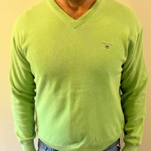 Ljusgrön tröja från Gant - Snygg ljusgrön stickad tröja från Gant med v-ringad hals och diskret broderad logga på bröstet. Tröjan har långa ärmar och ribbade muddar för en clean look. Perfekt för dig som gillar stilrena och fräscha färger. Tröjan har några små blekningsfläckar (som syns på bild 4-5) de syns knappt men bara så man är medveten☺️