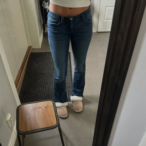 Blå bootcut jeans med låg midja - Blå bootcut-jeans med låg midja med snygga silvriga detaljer på bakfickorna. Materialet är stretchigt och formar sig efter kroppen. 