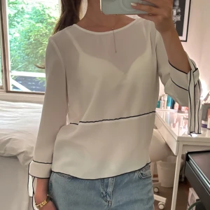 Vit blus med svarta detaljer - Stilren vit blus med svarta detaljer och trekvartsärm med knytband 🤍Supersnygg!