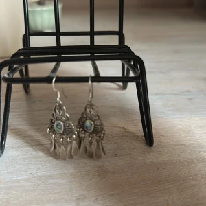 Silvriga boho örhängen med pärldetalj - Unika silvriga örhängen i boho-stil med vackra snirkliga detaljer och en skimrande pärla i mitten. Hängande droppformade hängen ger extra rörelse och cool vintagekänsla. Perfekta för dig som gillar statement-smycken med lite extra edge.