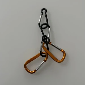 Set med svarta och orange karbinhakar - Säljer ett set med fem karbinhakar i metall, tre svarta och två i metallic orange. Perfekta att fästa på väskor eller ryggsäckar för att hänga nycklar eller accessoarer. Snygg och enkel design med silverfärgade öppningar.
