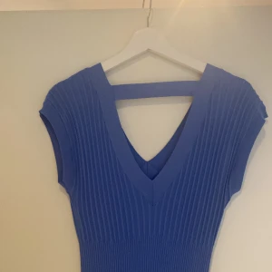 Blå ribbad klänning med v-ringning - Supersnygg blå klänning med ribbad struktur och v-ringad hals. Modellen är ärmlös och har en figurnära passform som framhäver siluetten. Perfekt för dig som gillar stilrena och moderna plagg med det lilla extra.