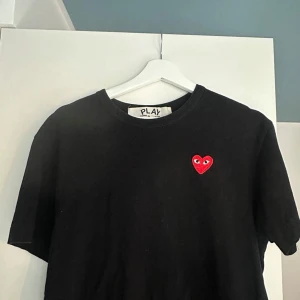 Svart Comme des Garçons Play t-shirt - Svart t-shirt från Comme des Garçons Play med det ikoniska röda hjärtat med ögon broderat på bröstet. Klassisk rund hals och korta ärmar. Tillverkad i mjuk bomull för en skön känsla och clean look. Ordinarie pris 1200 kr.
