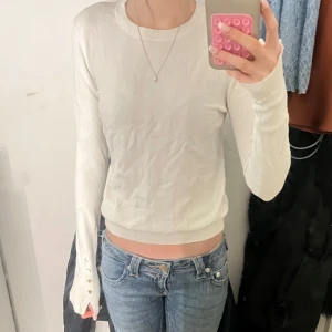 Vit långärmad tröja med knappar - Säljer en stilren vit långärmad tröja med rund halsringning. Tröjan har snygga knappdetaljer vid ärmsluten och en tight passform som sitter snyggt till jeans eller kjol. Perfekt för dig som gillar en clean och enkel look. Priset kan diskuteras 💗
