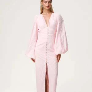 Adoore positiano dress - Superfin ljusrosa långklänning från adoore med djup v-ringning, puffiga långärmar och knappar framtill. Klänningen har en slits framtill och är sydd i ett lätt, blommigt tyg som ger en romantisk känsla. Perfekt för dig som vill sticka ut med en elegant och feminin look. Endast använd en gång och är i mycket bra skick 