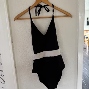 Svart och vit baddräkt med knyt - Säljer en svart baddräkt med vit rand över midjan och band som knyts i nacken. Den är v-ringad fram. Perfekt för stranden eller poolen. Använd max 5 ggr för ca 2år sedan. Och är nytvättad! Tror den är från Esprit men det står inget på lappen tyvärr. Läs gärna bio💕