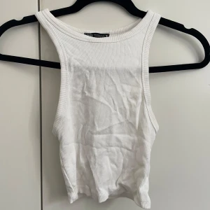 Vit ribbad linnetopp från Zara - Säljer en fräsch vit ribbad linnetopp från Zara. Toppen är ärmlös med rund halsringning och croppad passform, perfekt till jeans eller kjol. Enkel och stilren design som funkar till många olika looks.