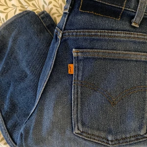 Levi's 501 blå jeans straight fit - Klassiska blå Levi's 501 jeans med raka ben och orange etikett på bakfickan. Jeansen har fem fickor, snygga kontrastsömmar och är tillverkade i slitstarkt bomullsdenim. Perfekta för dig som gillar tidlös och avslappnad stil.