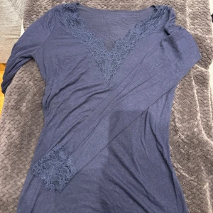 Mörkblå långärmad topp med spets Intimissimi  - Mörkblå långärmad topp med djup v-ringning dekorerad med spetsdetaljer, ifrån intimissimi  Även ärmsluten har matchande spets. Tunn och mjuk i materialet, perfekt för lager-på-lager eller som statement-piece. Snygg och stilren för dig som gillar detaljer.